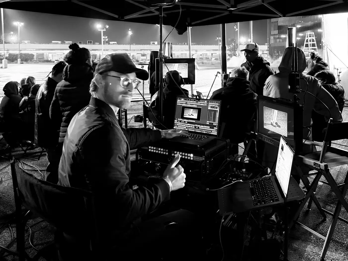 Morgan Spadone at a video-assist cart on a night exterior set, monitors and routing gear in front of him.