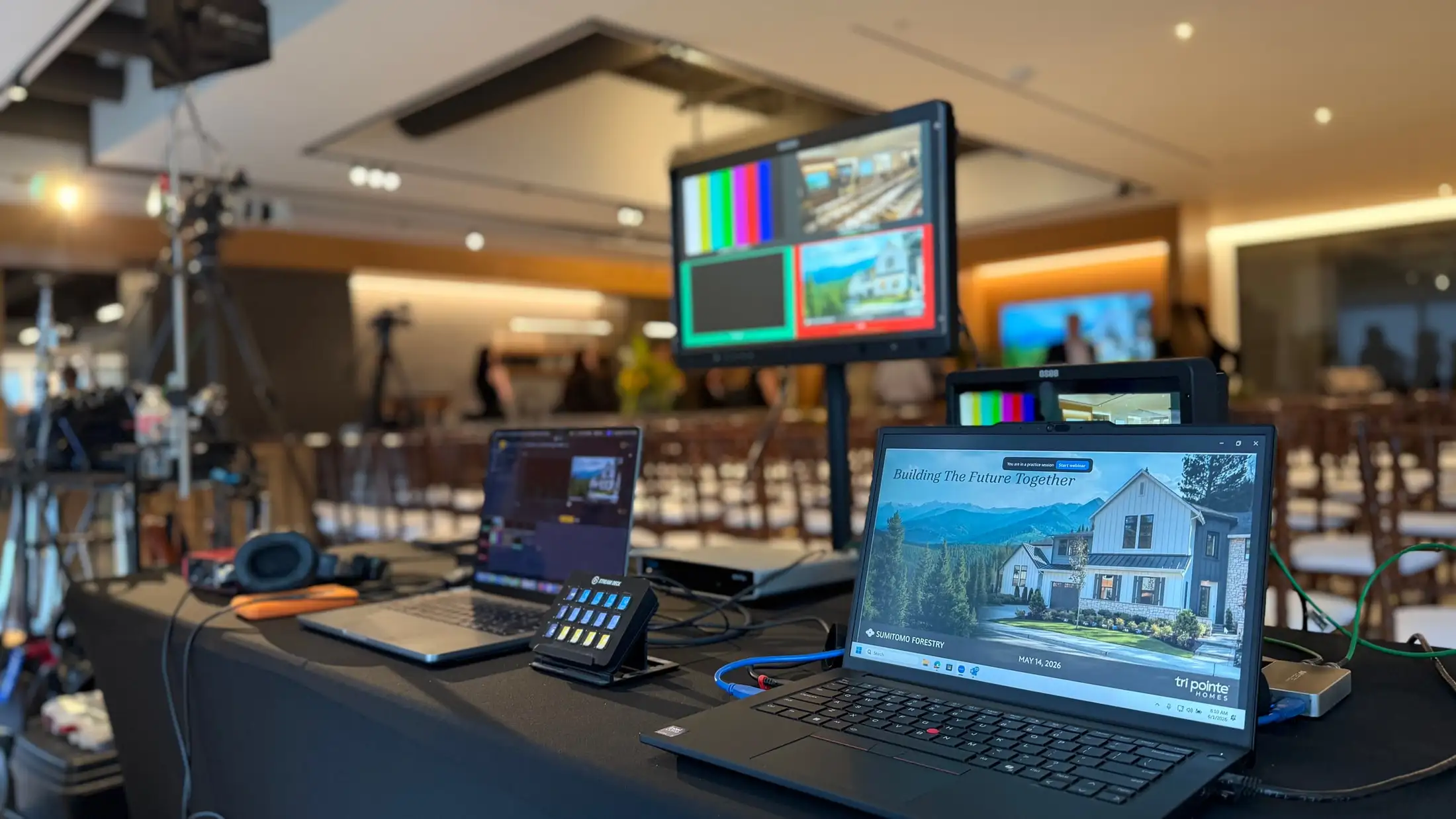 Live event production position showing a multiview monitor, presentation laptop, and control surface at the rear of an event space.