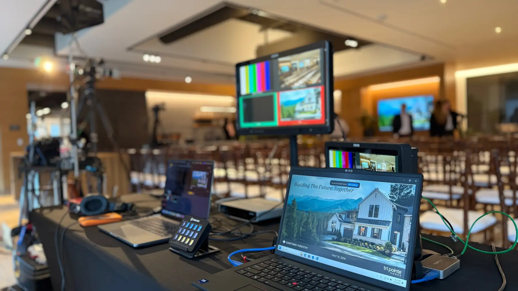 Live production control surface and monitoring set up on a table at the back of an event space.